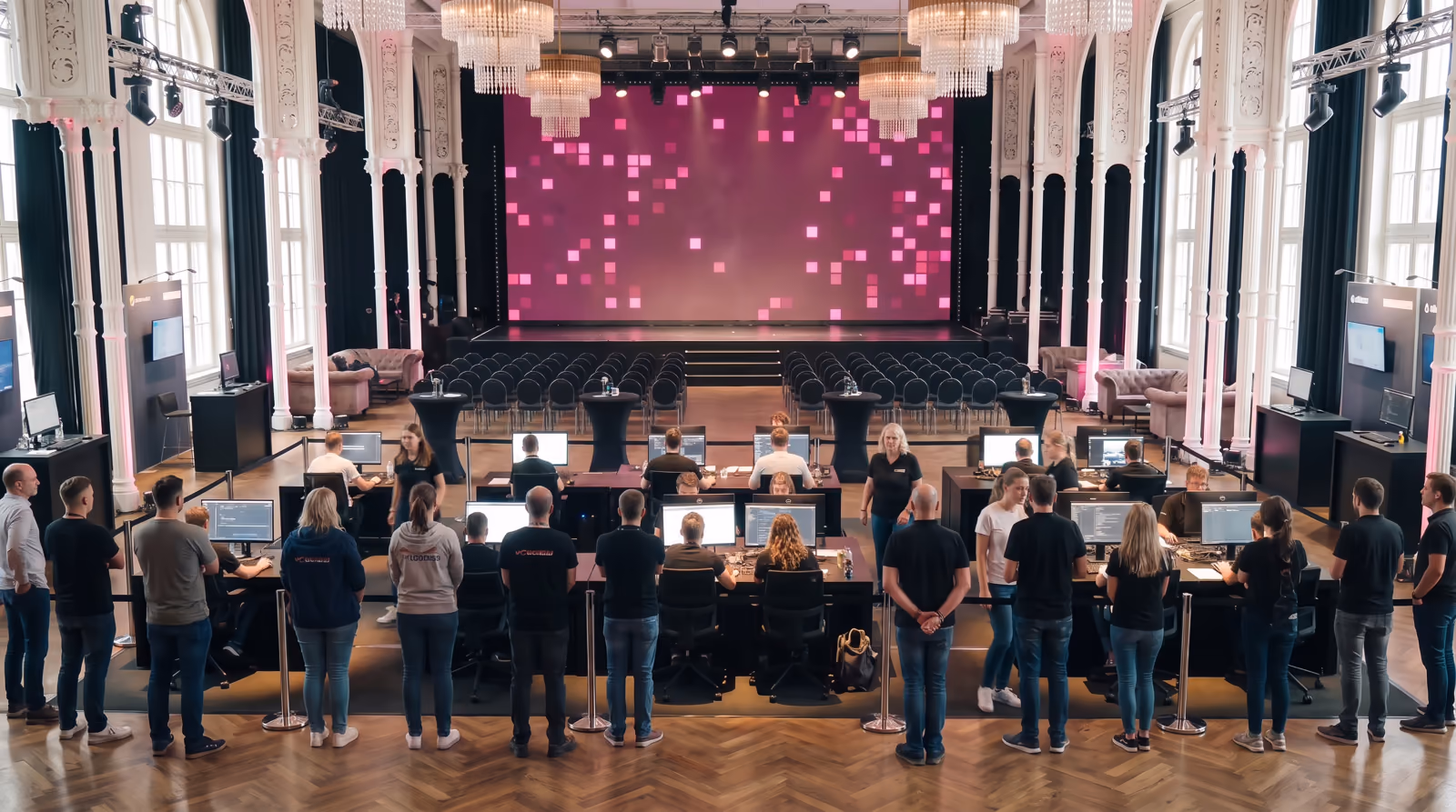 Der Festsaal der Flora bei Tageslicht: Die Teilnehmenden bauen an ihren Bildschirmen, ihre Leute stehen dahinter, vorn leuchtet die LED-Wand magenta. KI-Visualisierung des geplanten Tages. Basis: echtes Foto der Flora Köln.